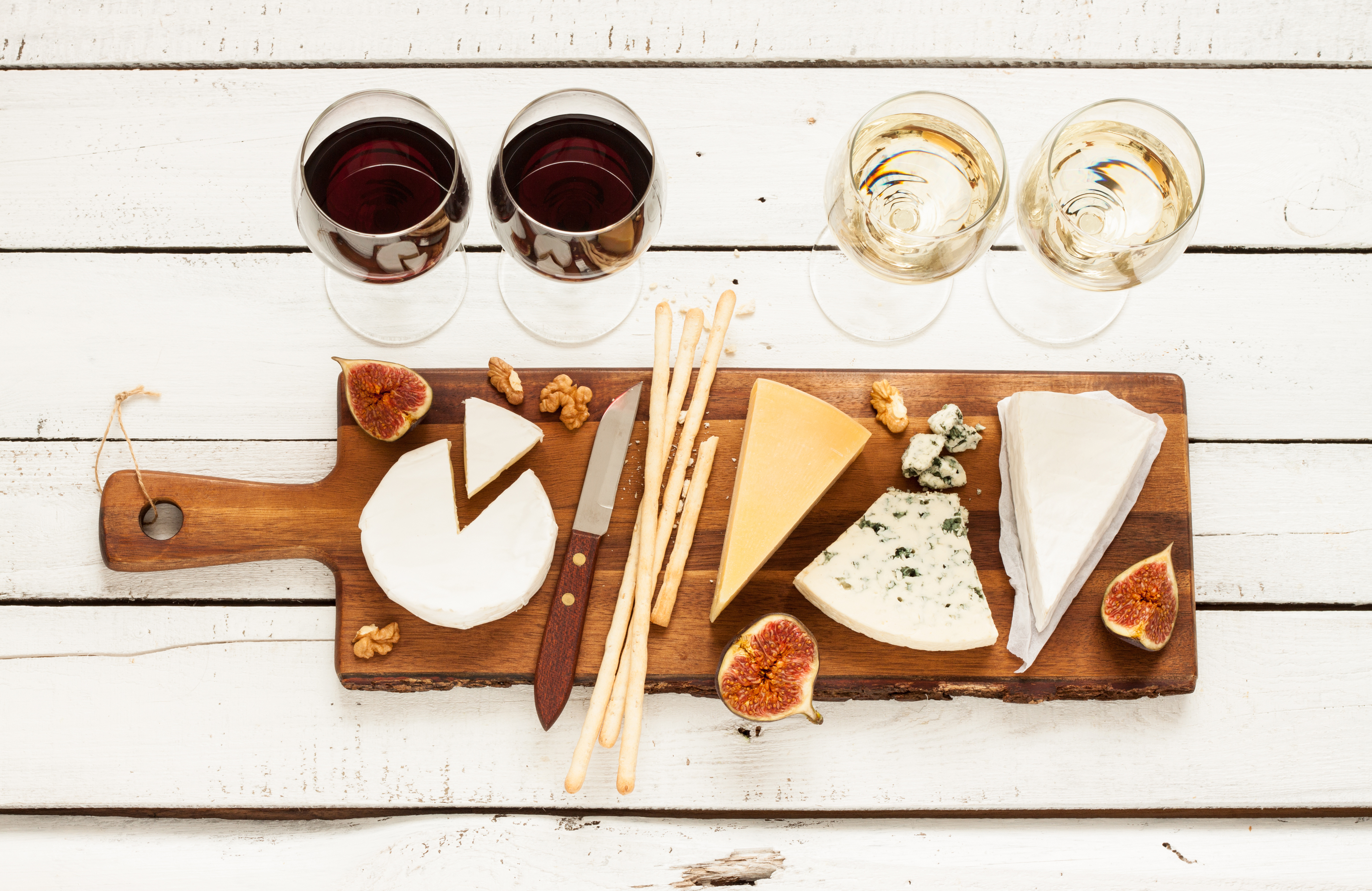 Red and white wine plus different kinds of cheeses (cheeseboard) on rustic wooden table