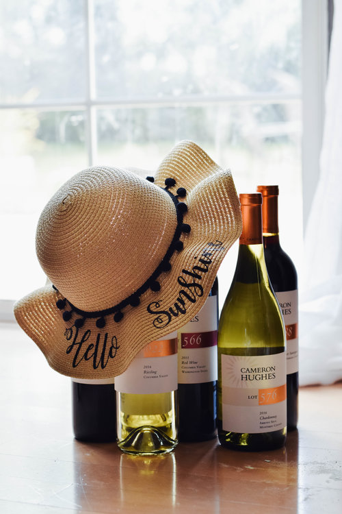 Sun hat laid over the top of Cameron Hughes wine bottles with a mix of red and white wines