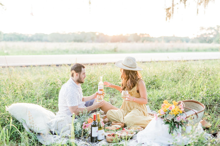 A couple glamping, seated on a picnic table enjoying a wine-paired picnic meal
