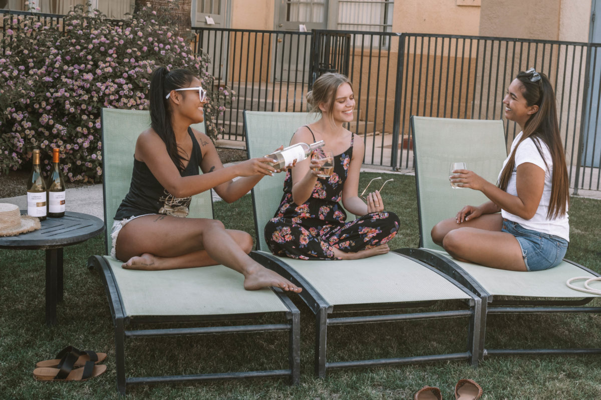 Three female friends on poolside lounge chairs enjoying wine