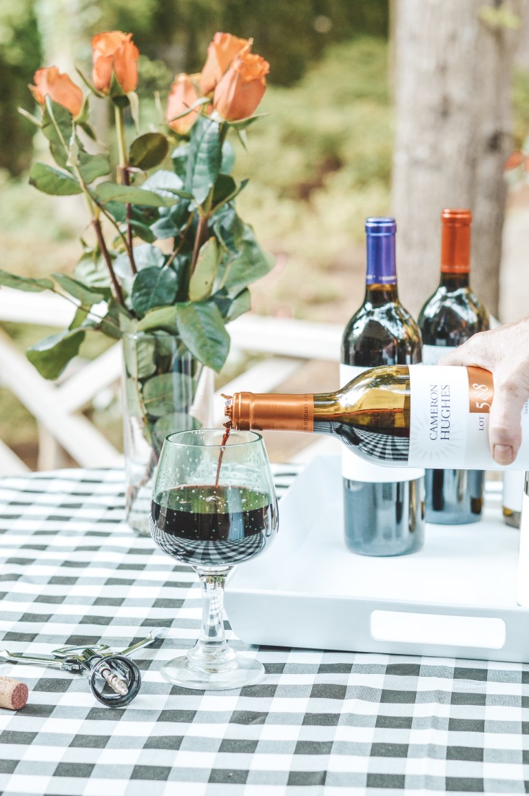 Wine being poured into a glass on a picnic table with fresh flower centerpiece