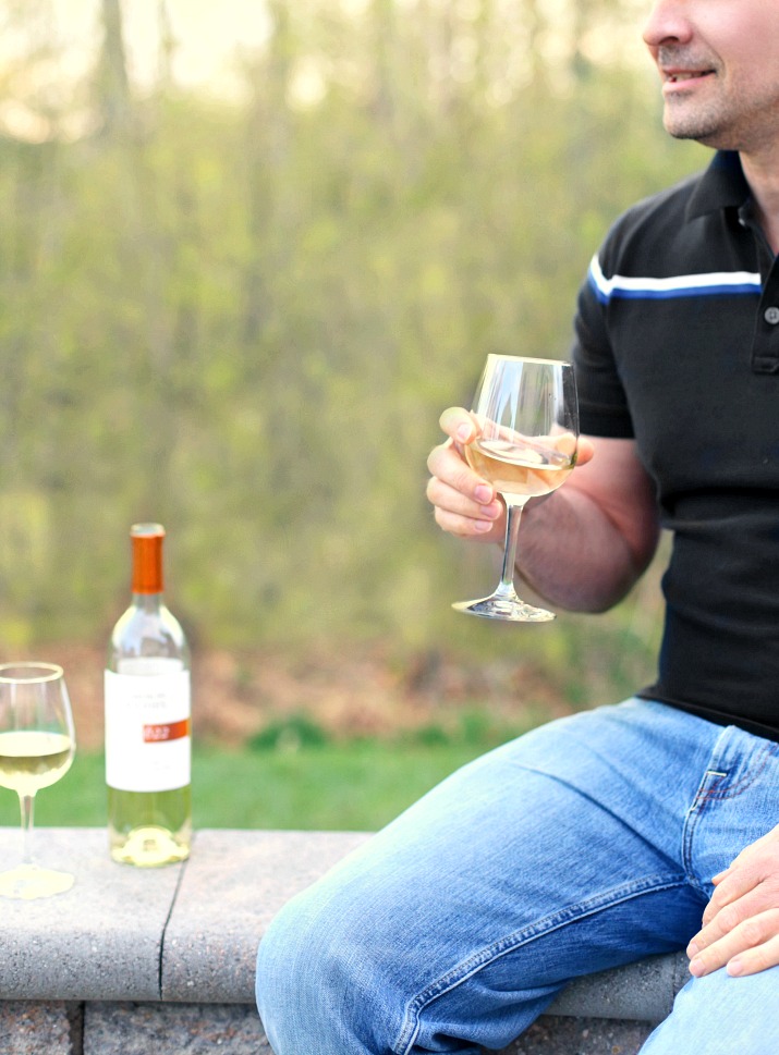 A man enjoying a glass of Cameron Hughes white wine sitting on an outdoor wall