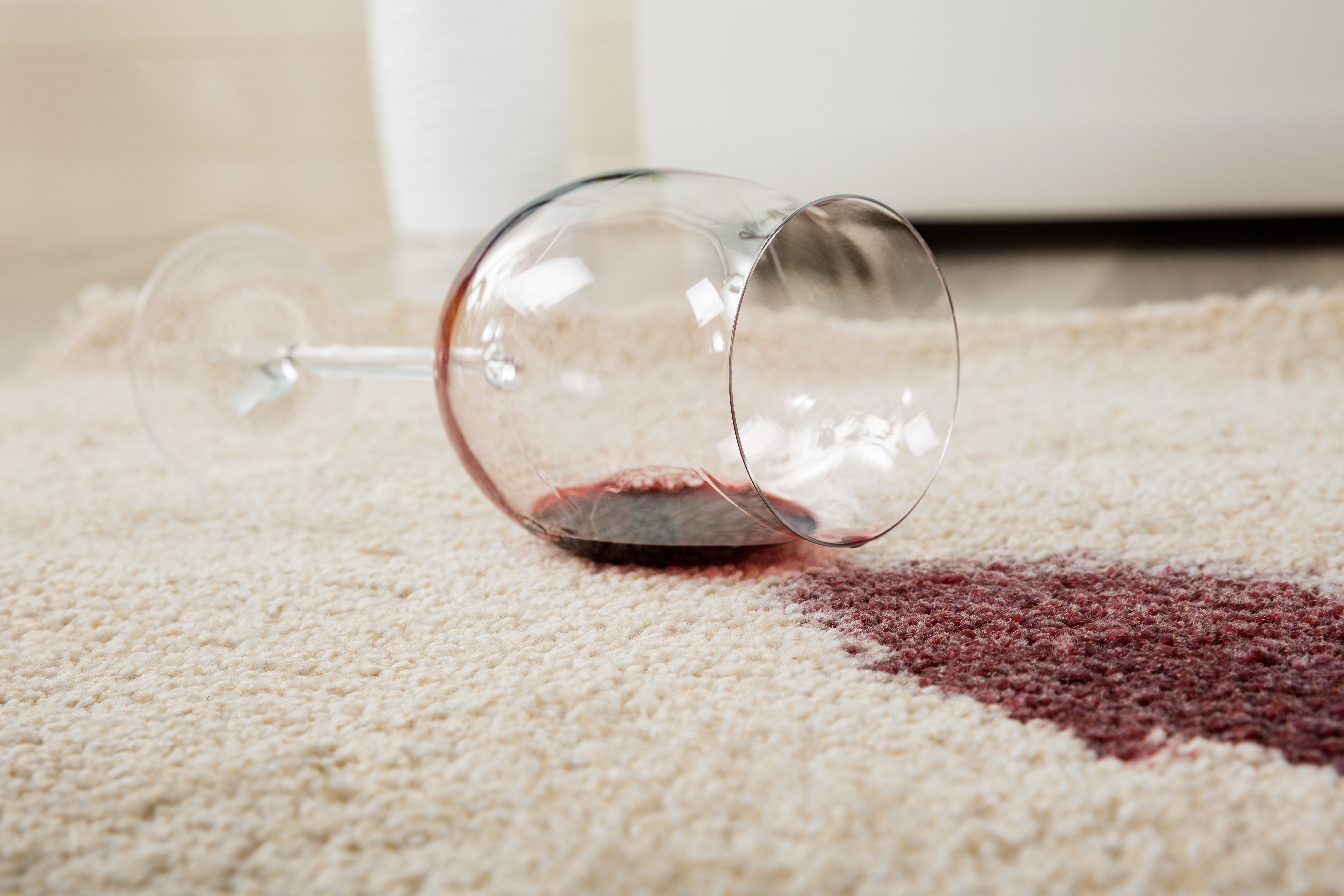 Red wine spilling on a light colored carpet to illustrate methods to clean stains