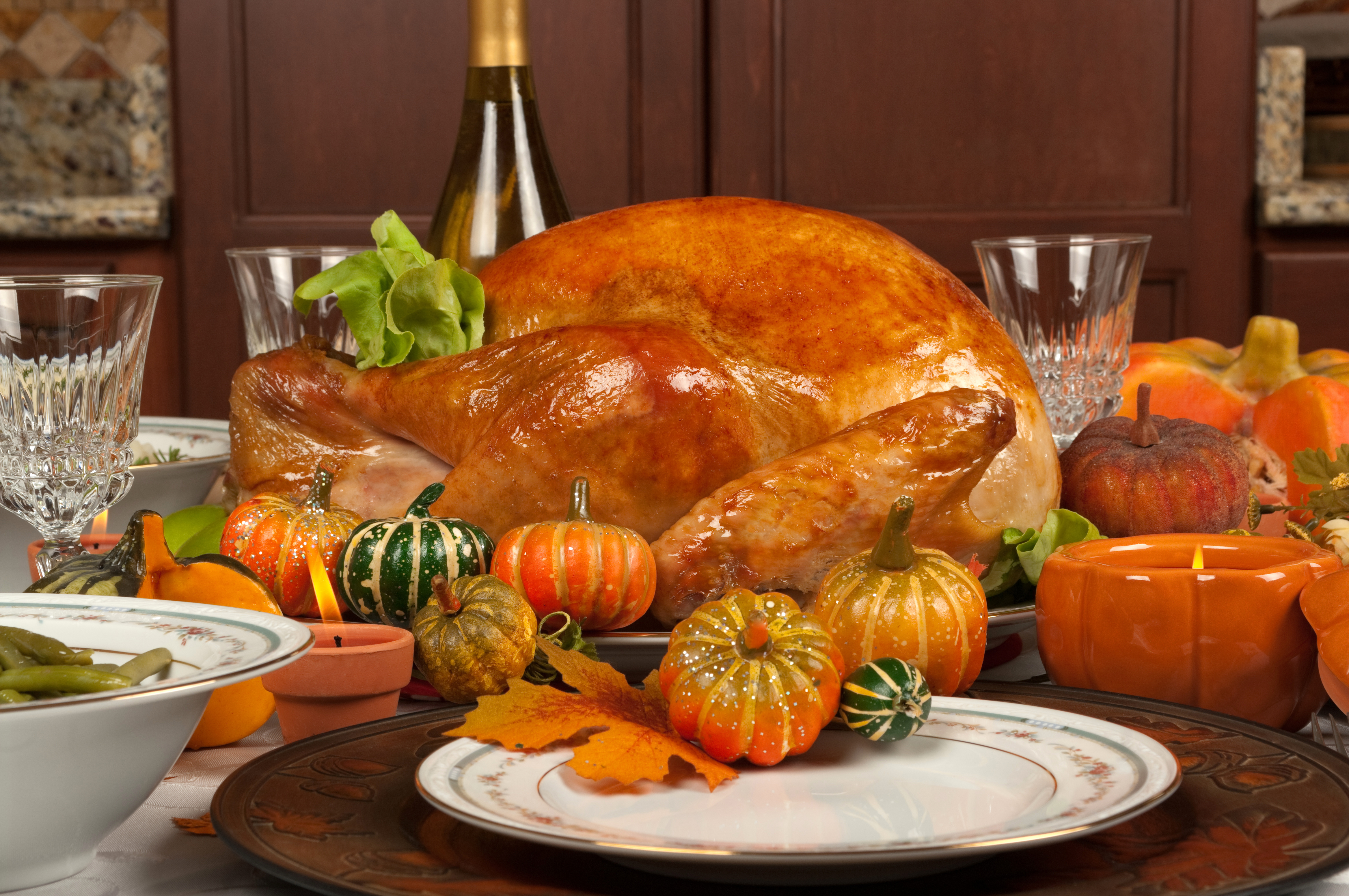 Thanksgiving turkey on a table with a full setting including holiday-inspired pumpkins and gourds and of course wine