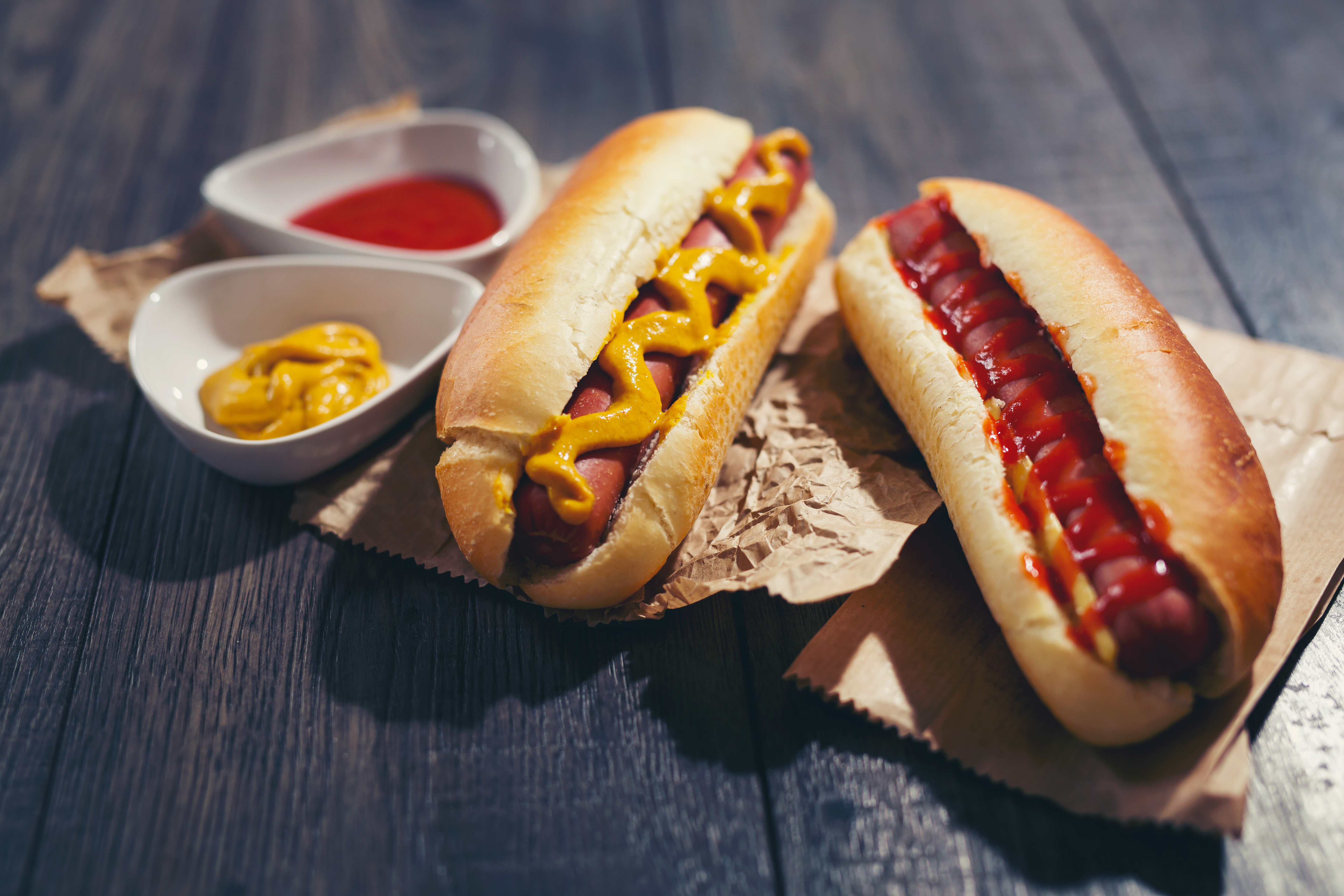Tasty hot dogs with ketchup and mustard on paper on wooden background