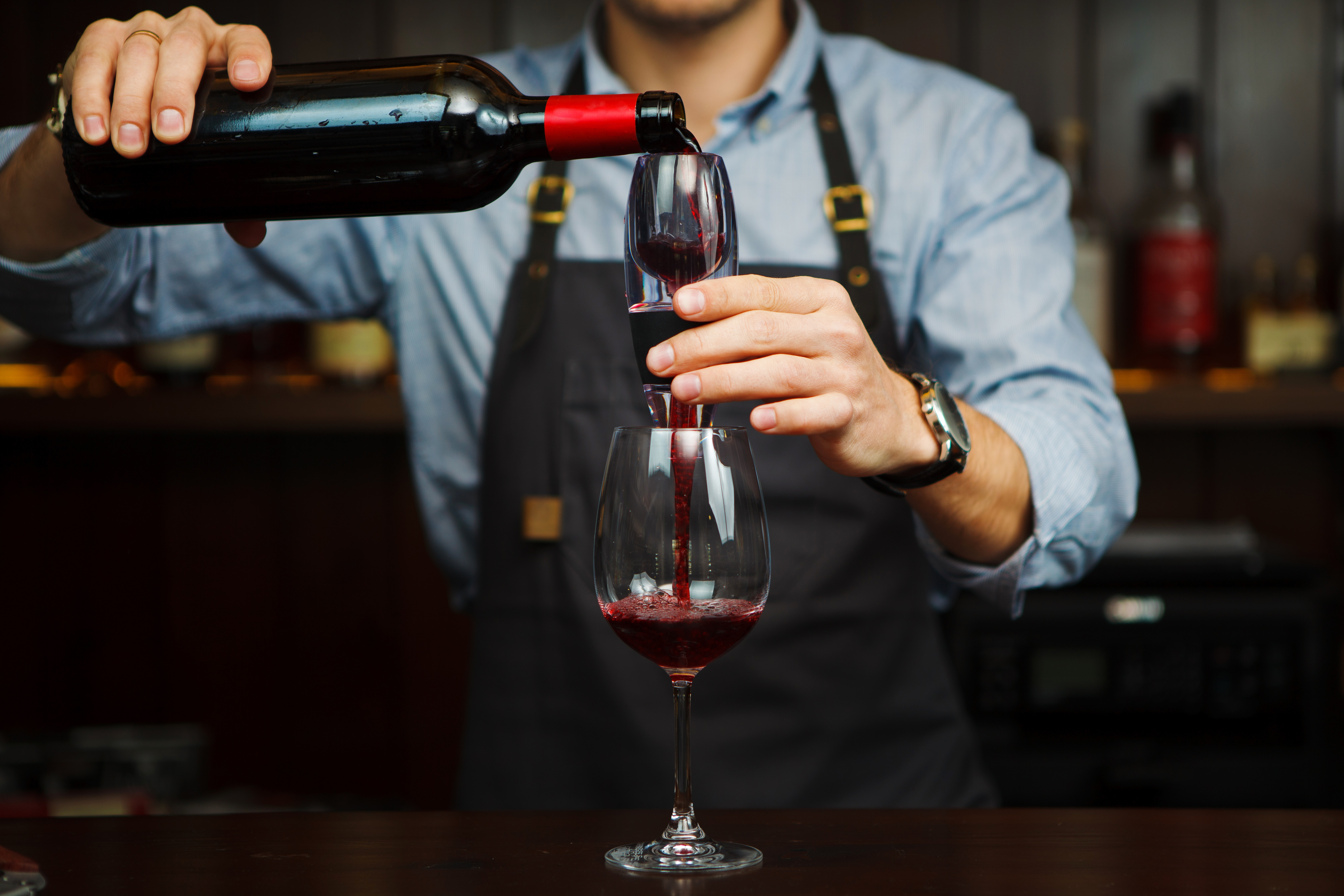 Male sommelier pouring red wine through aerator into glass.