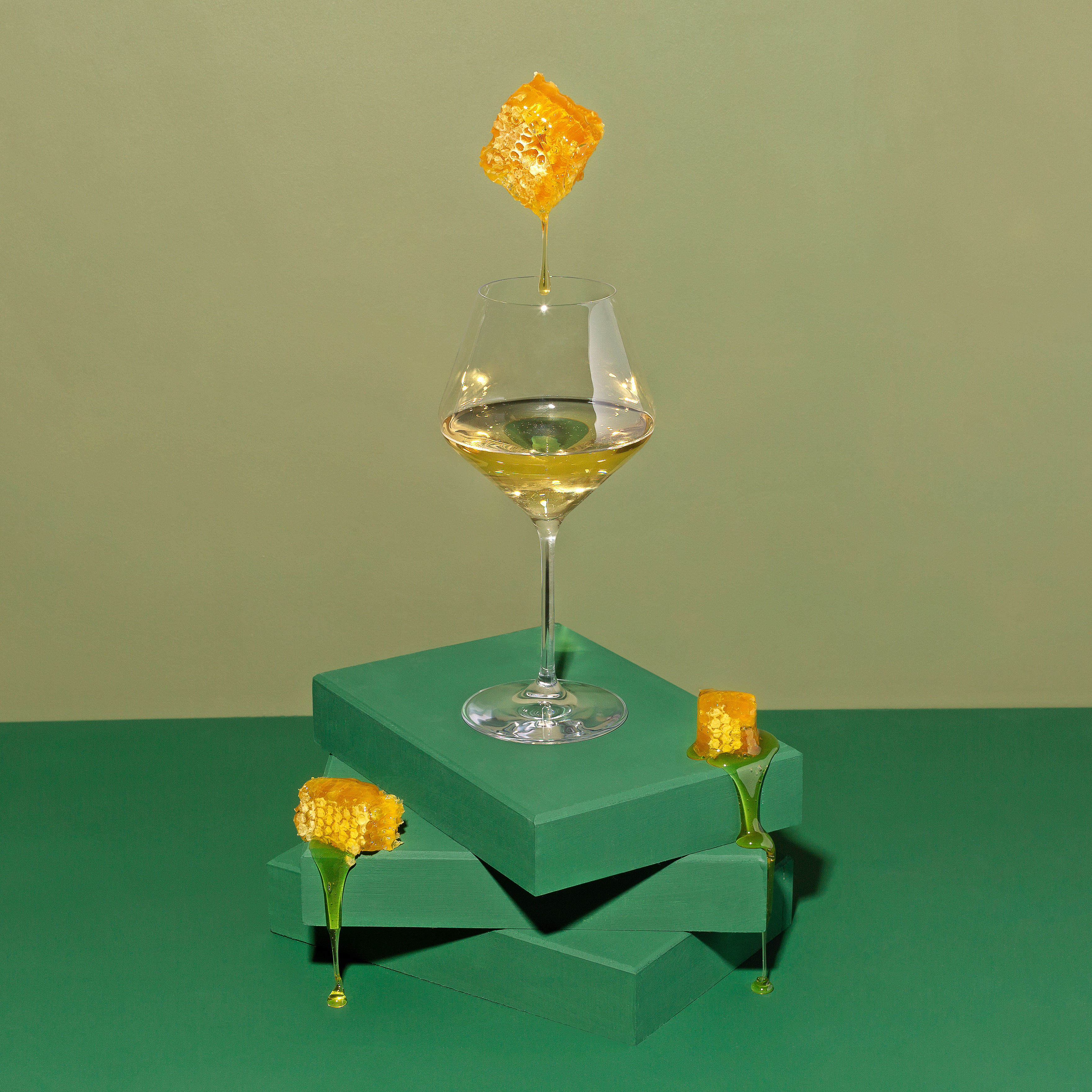 Balancing act with a white wine glass and a honeycomb hovering above and dripping honey into the wine glass