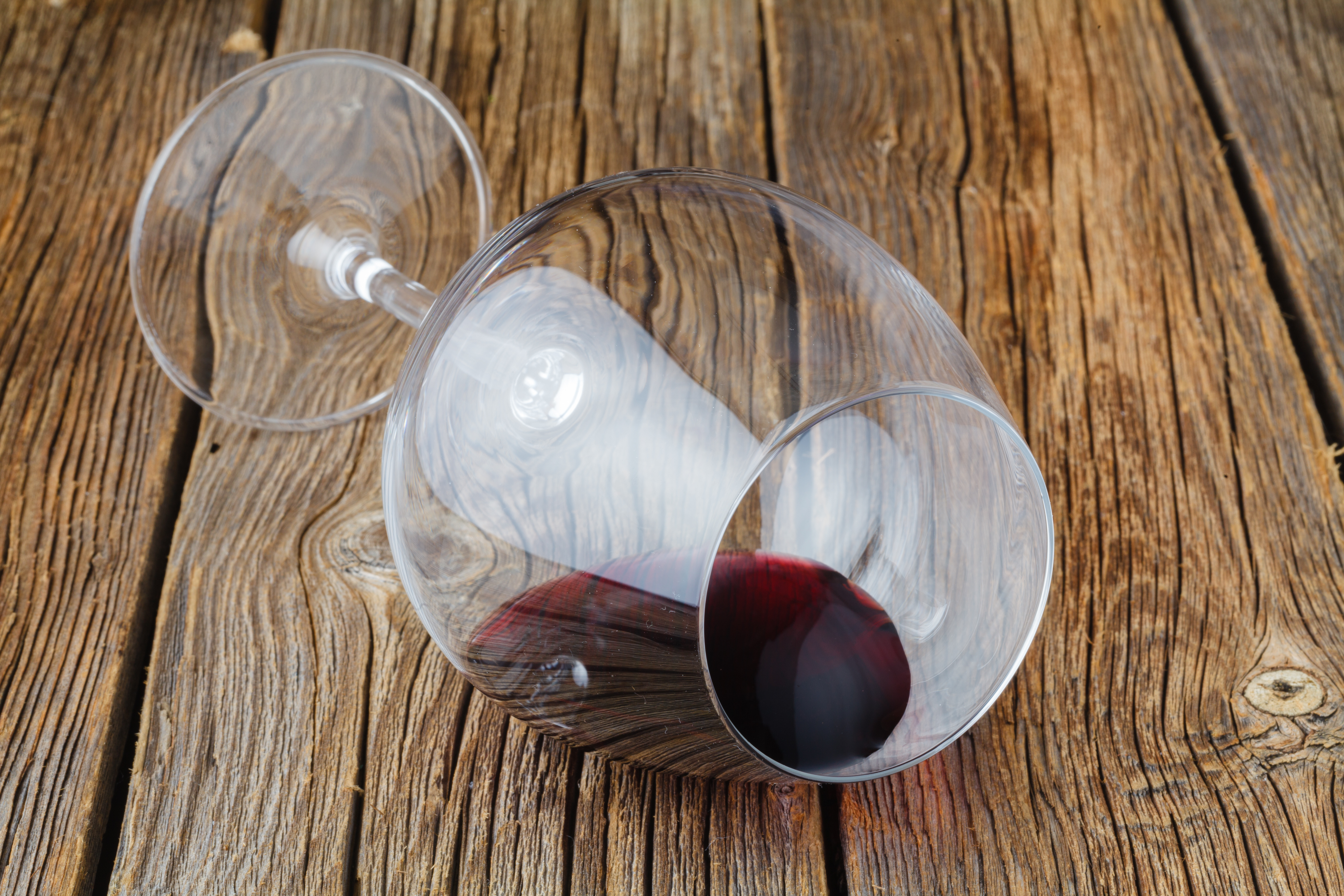 One glass Half of red wine on wooden table laid on its side with the wine staying inside the glass