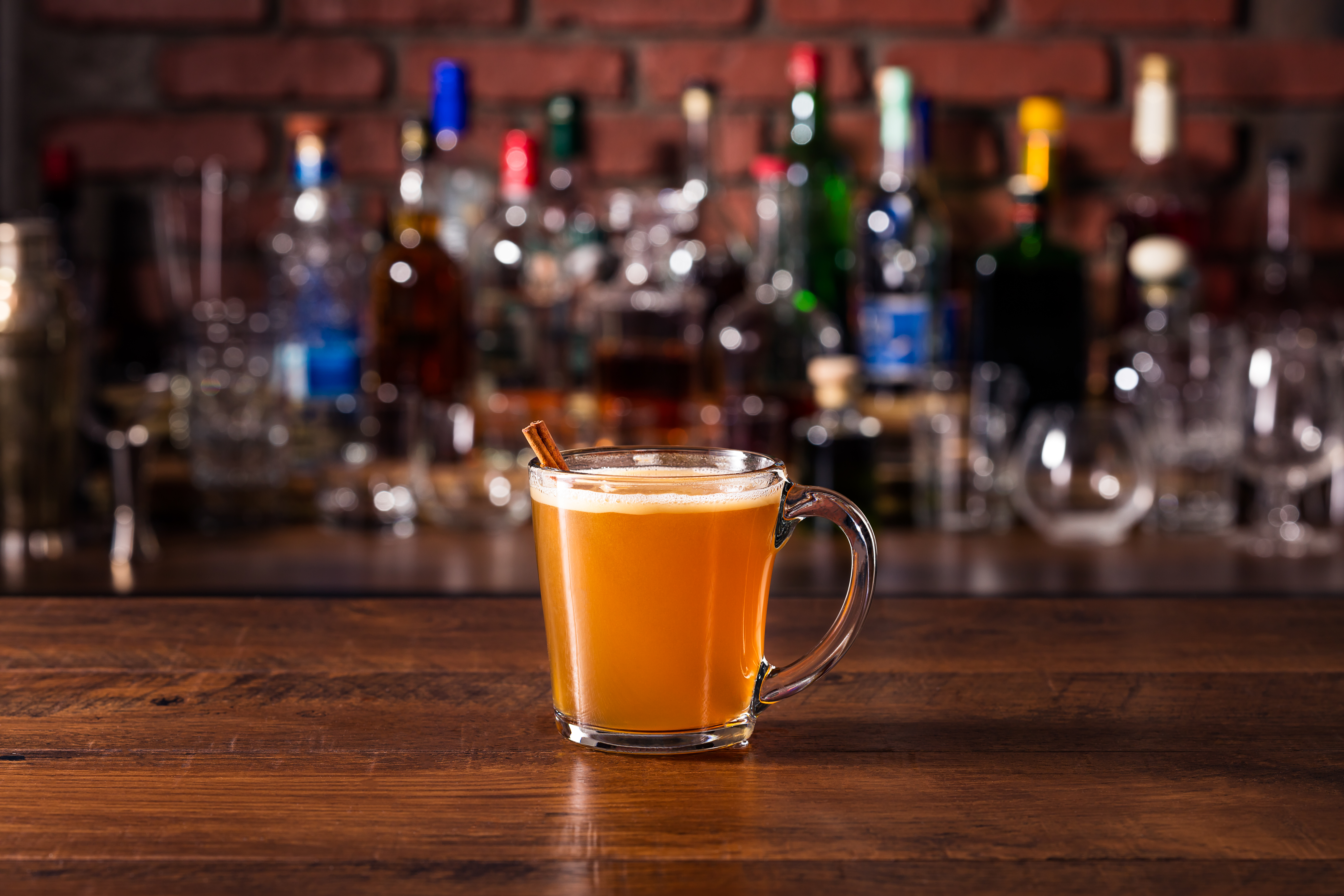 Warm Whiskey Hot Buttered Rum on a bar with various alcohol bottles in the background