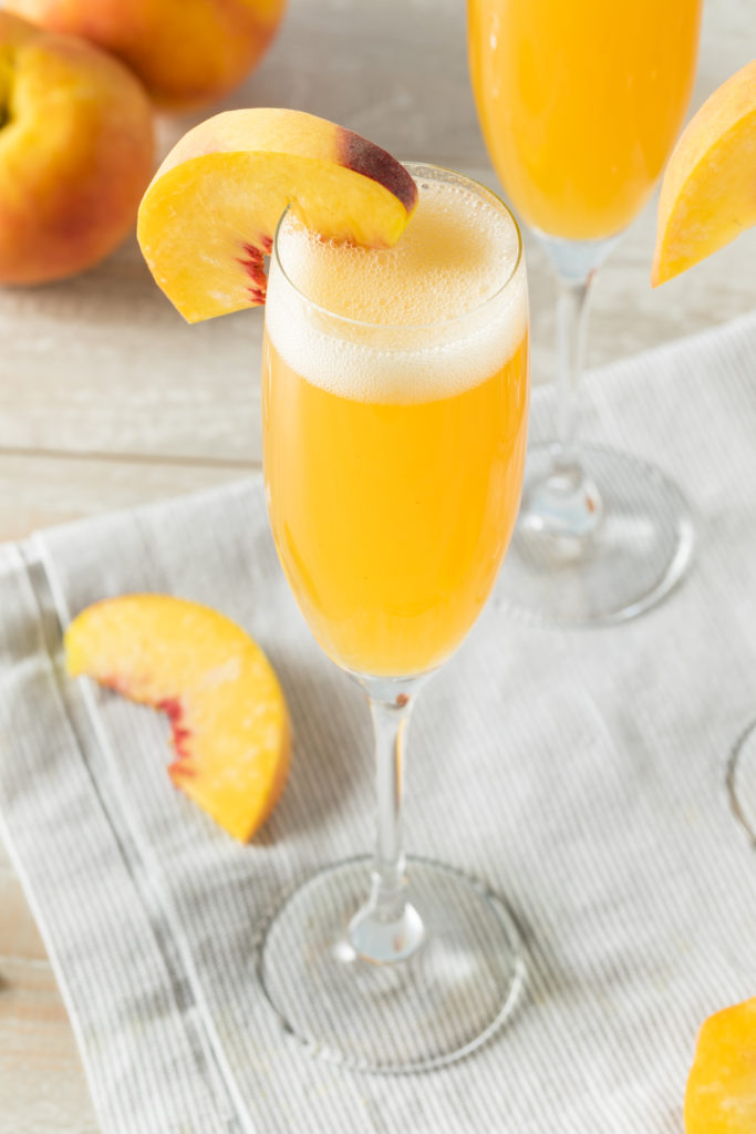 Mixed fruit cocktail with Prosecco and peach wedge garnish
